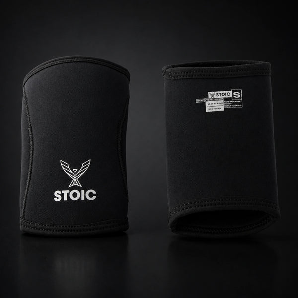 Stoic 7mm elbow sleeves for weightlifting in black, the pair standing side by side, one showing the phoenix logo on its front and the other showing the printed size and care label.