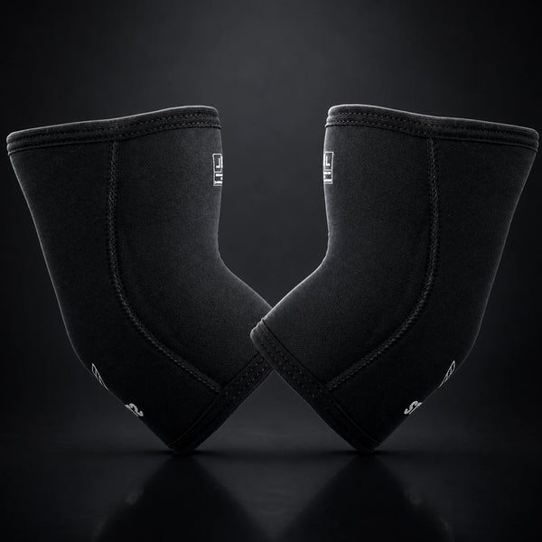 Stoic 7mm elbow sleeves for weightlifting in black, the mirrored pair standing on their narrow ends, showing the tapered anatomical shape and curved seam.