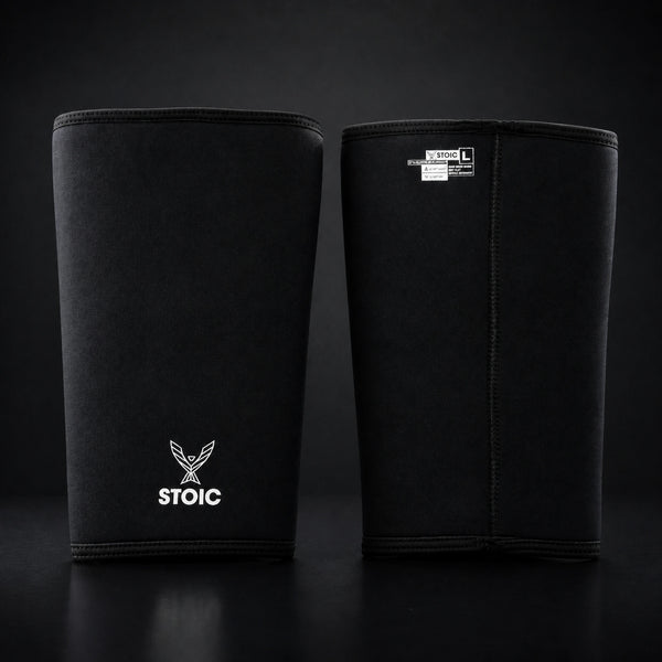 Stoic 7mm knee sleeves for weightlifting in black, the pair standing side by side, one showing the phoenix logo on its front and the other showing the woven size and care label.