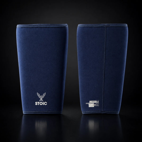 Stoic 7mm knee sleeves for weightlifting in navy, the pair standing side by side, one showing the phoenix logo on its front and the other showing the woven size and care label.