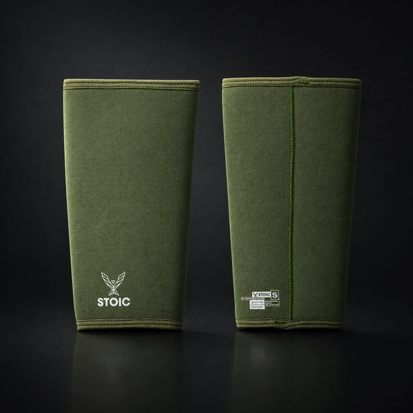 Stoic 7mm knee sleeves for weightlifting in olive drab, the pair standing side by side, one showing the phoenix logo on its front and the other showing the woven size and care label.