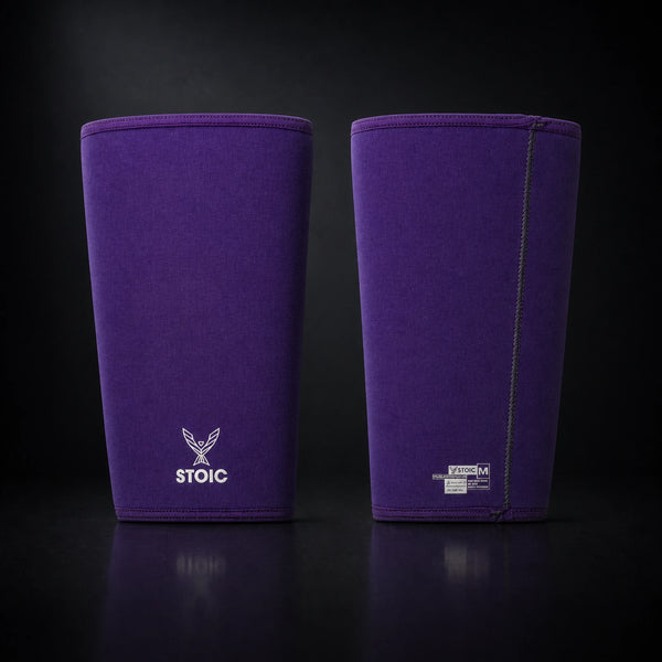 Stoic 7mm knee sleeves for weightlifting in purple, the pair standing side by side, one showing the phoenix logo on its front and the other showing the woven size and care label.