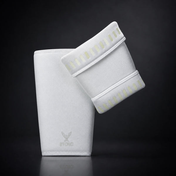 Stoic 7mm knee sleeves for weightlifting in white, the pair arranged with one sleeve showing the phoenix logo on its front and the other turned to reveal the silicone grip dashes inside the cuffs.