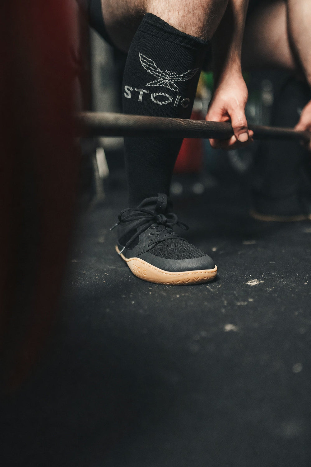 Stoic Barefoot Trainer — matte zero-drop minimalist lifting shoe with gum sole, on a gym platform mid-deadlift