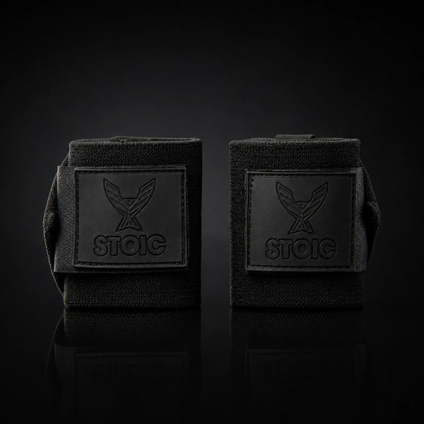 Stoic wrist wraps for weightlifting in Black Label, two rolled wraps standing apart, both logo patches facing the camera.
