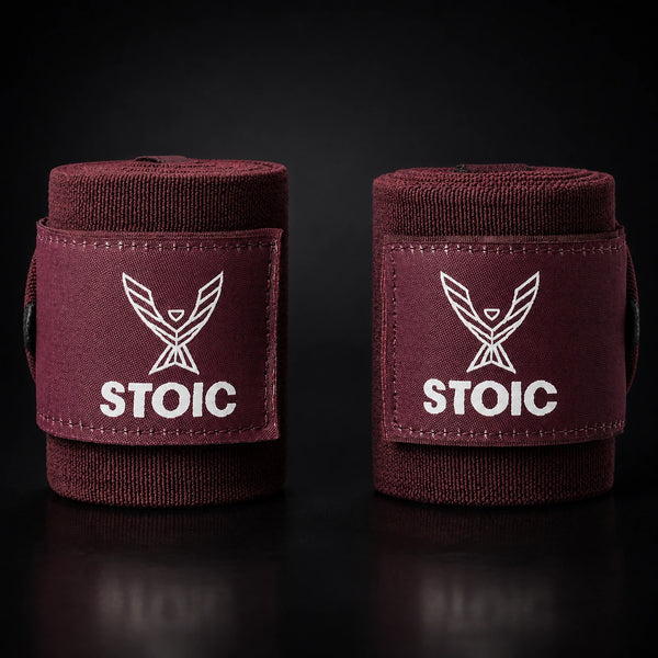 Stoic wrist wraps for weightlifting in maroon, two rolled wraps standing apart, both logo patches facing the camera.