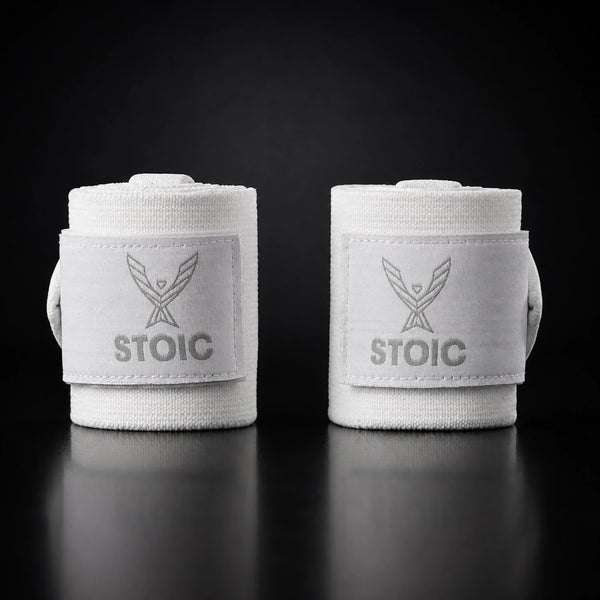 Stoic wrist wraps for weightlifting in white, two rolled wraps standing apart, both logo patches facing the camera.